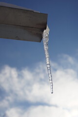 Huge long icicle hang on a drainpipe of a house. Background blue