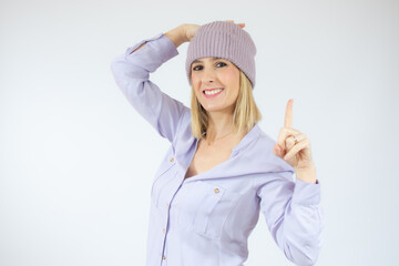 Portrait of a happy young woman wearing winter hat pointing finger up at copy space isolated over white background