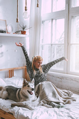 Funny Blond girl lies on the bed with a white husky dog. Sunny morning