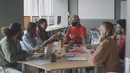 Team of multiethnic colleagues in protective face masks discussing business project while having office meeting during coronavirus pandemic - Powered by Adobe