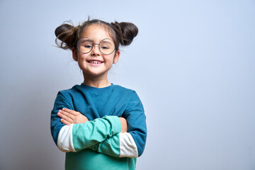 Portrait of cute swarthy caucasian little girl with glasses, arms crossed and funny hairstyle,...