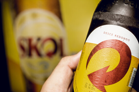 Cerveja Skol. Homem segurando uma garrafa de cerveja da marca Skol em close up.