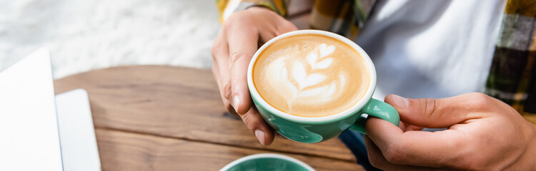 cropped of man holding cup of coffee with latte art, banner