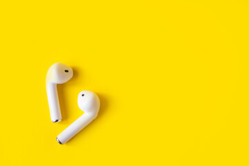 Wireless white headphones on a yellow background, place for text. Colorful summer concept