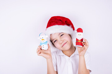 a boy in a Santa Claus hat holds Christmas crafts on a white background