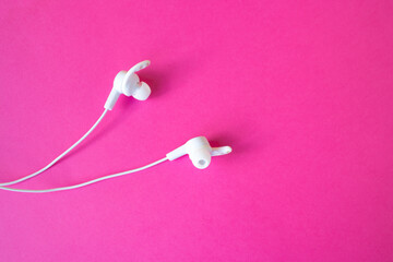 White headphones with a wire on a pinkbackground.