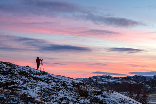 The photographer stands on a mountain against the background of the sky and takes a picture using a tripod. Bright dawn.