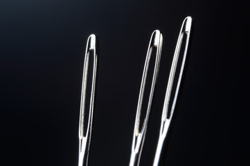 three sewing needles without thread on a dark background. macro.