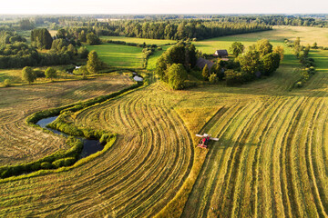 An aerial of a tractor cutting grass on a meadow next to a river during a beautiful summer evening in Estonian countryside. 