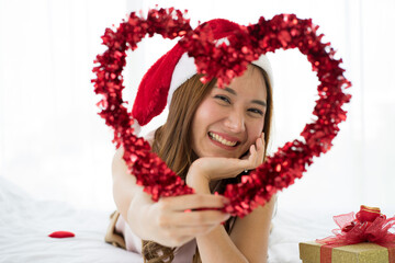 Obraz na płótnie Canvas Asian beautiful young woman wearing Santa hat on white bed with red gift box for Christmas holiday festival. 