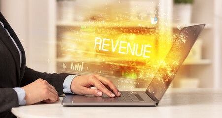 Closeup of businessman hands working on laptop with REVENUE inscription, succesfull business concept