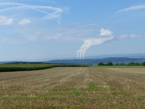 Abgeerntete Getreidefelder mit Türmen und Rauchsäule des Kernkraftwerk Cattenom am Horizont