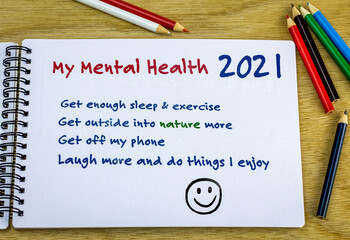 Mental health resolutions 2021 heading with list of ideas hand written in note book on desk. New...