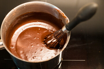 Preparing delicious hot chocolate with a whisk in a metal saucepan. Close up shot of traditional recipe, top view.
