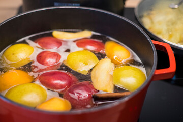 Preparing delicious hot apple cider with cinnamon in a red pan. Close up shot of festive recipe.