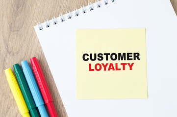 Customer Loyalty text written on a notebook with colored markers on a wooden table