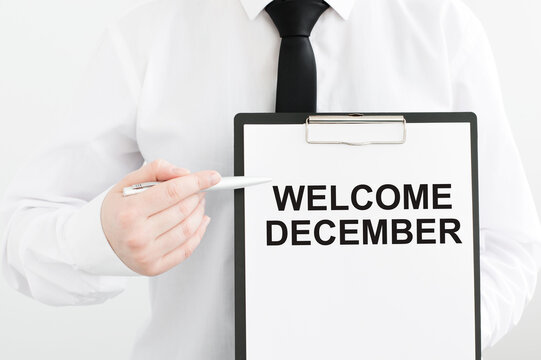 businessman in a white shirt holds a tablet with the inscription welcome december on a gray background