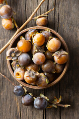 Ripe small persimmon fruit, black date or palm berries with branch on wooden background, (Diospyros lotus), copy space for text