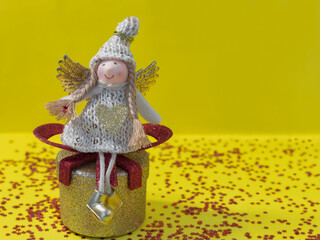 Photo-postcard of an angel girl who sits on a gold gift on a yellow background with red sparkles. Minimal concept of Christmas and New Year