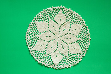 light knitted round lace doily on a green background close up