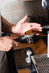 cropped of tattooed barista holding portafilter with roasted ground coffee