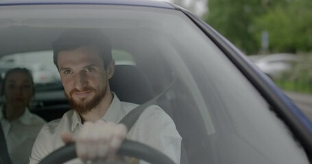 Happy young taxi driver in car with female passenger on backseat