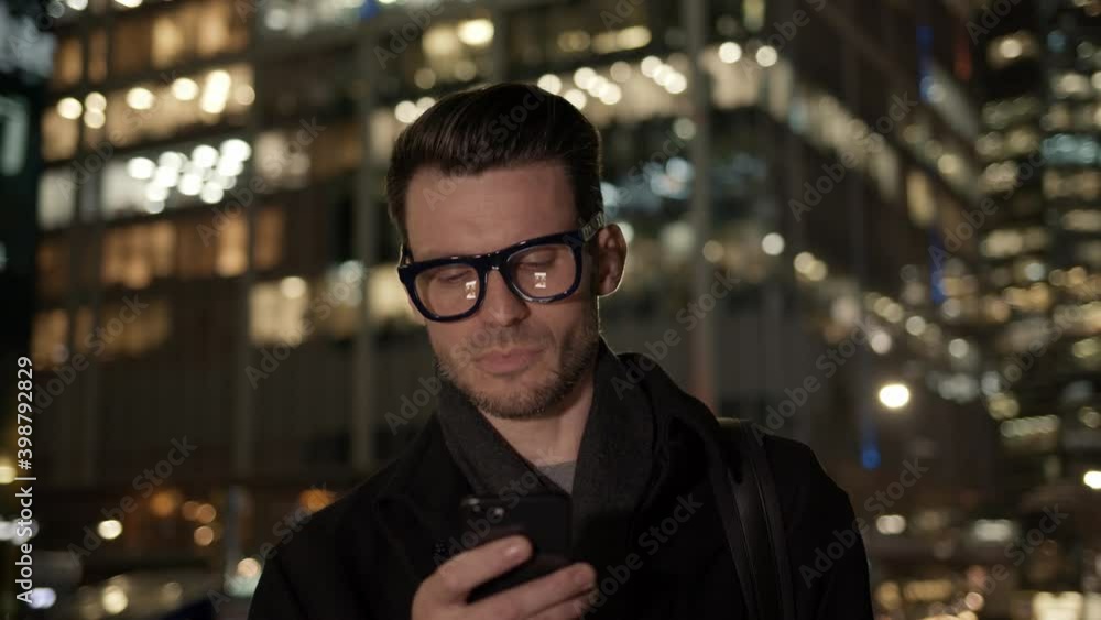 Poster man in eyeglasses with phone in hand on background of building with lights on. gimbal night shot of 
