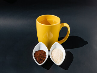 Taza amarilla con agua, contenedores con azúcar y café para preparar bebida