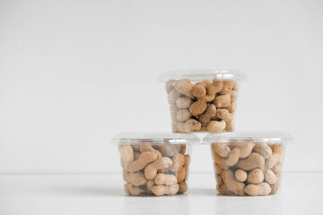 Inshell peanuts in three transparent plastic bowls on a white table. Copy, empty space for text