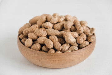 Dry peanuts in shell in a wooden bowl on a white background. Copy, empty space for text