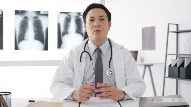 Young Asia male doctor in white medical uniform with stethoscope using computer laptop talk video conference call with patient, looking at camera in health hospital. Consulting and therapy concept.