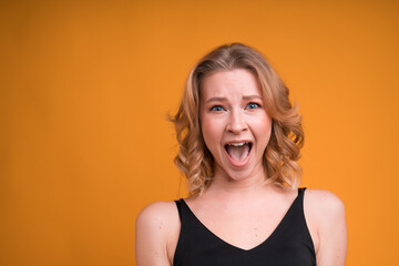 Portrait of a blonde girl with an open mouth laughing on an orange background