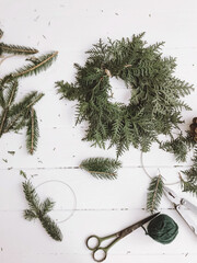 Making christmas rustic wreath, cedar and fir branches with scissors on white wooden rustic table