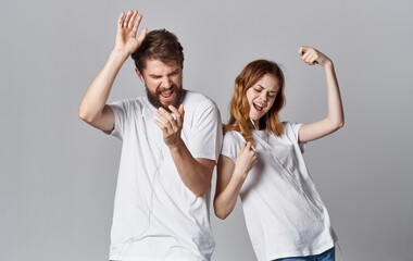 cheerful man and woman in headphones listen to music and dance on a gray background