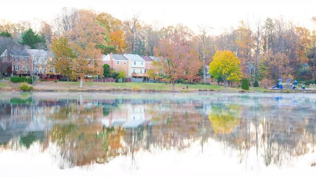 Timelapse of sunrise on Braddock lake in Burke, Virginia, USA, Fairfax county with reflection of townhouses, fog and mist floating above on water surface in autumn fall loopable cinemagraph