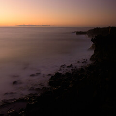 Coastal landscape long exposure photography of the sunrise in a rocky cliff in Candelaria, Tenerife, Canary Islands, Atlantic Ocean. Silk effect on water.