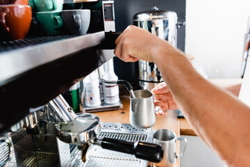 Cropped of barista holding metallic milk mug near steamer of coffee machine