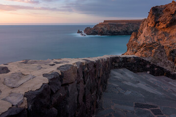 Coastal, sunset, long exposure landscape with warm sky and clouds. Stone stairway leading to a cliff in San Marcos beach, Tenerife, Spain.