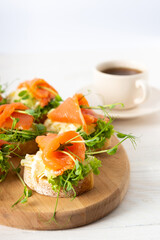 Canapes with mozzarella cheese, salad, salmon and pea sprouts, toast with red fish on a wooden board close up