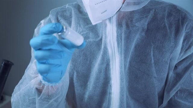 Scientist holding ampule with white powder, illegal pharmacy production, drugs. Laboratory assistant examines glass medical ampoule for injection. Penicillin dry powder medicine. Antibiotic injection