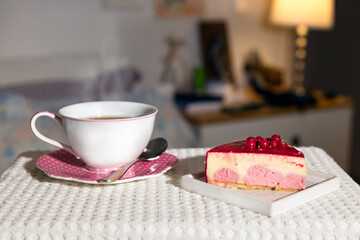 Red berries and vanilla cream cake with a cup of tea - coffee over a cozy home background.