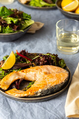 Fried salmon steak with salad in a plate , white wine in a glass, delicious hearty dinner or lunch