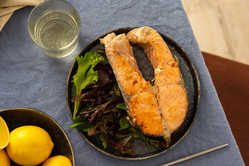 Fried salmon steak with salad in a plate , white wine in a glass, delicious hearty dinner or lunch