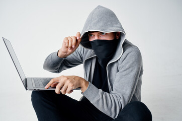 a man in a mask sits on the floor in front of a laptop computer hacking crime