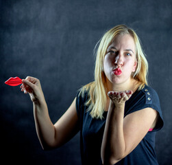 Caucasian blonde woman with red lipstick blowing a kiss while holding toy plastic lips