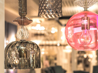 A group of switched-off multicolored lamps with a gray, pink glass ceiling is suspended in the white interior. Concept of hotel decoration. Indoors. Close up. Warm light.