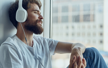 cute men sitting near the window wearing headphones music enjoyment