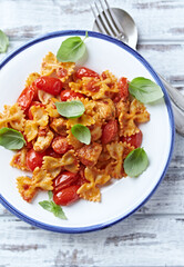 Farfalle pasta with chicken breast, cherry tomatoes and fresh basil. Bright wooden background. Top view.