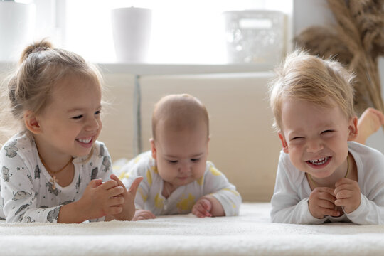 Three Little smiling kids play together on soft white bed at home. Brother and siste read book fairy tales with baby. Children meeting new born sibling.Toddlers laugh and bond. funny.Copy space