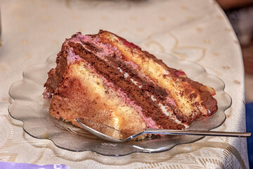 Close view of a delicate piece of chocolate cake, torte with nuts and fruits on a plate with a spoon.